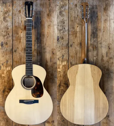 Front and back views of a new light-colored acoustic guitar against a rustic wooden wall.